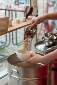A woman fills grains into a white bowl, detail from an unwrapped shop. A woman fills grains into a white bowl, detail from an unwrapped shop.